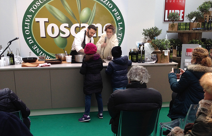 presentatrice con cuoco e due bambini al bancone di olio toscano igp